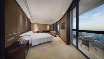 A modern hotel room with a large bed, a desk, and a view of the cityscape through large windows.