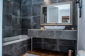 A modern bathroom with dark tiles, a white sink, and a large mirror.