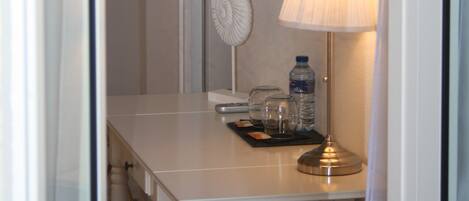 Habitación de hotel con una mesa blanca, una lámpara, una botella de agua, un vaso y un control remoto.