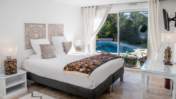 Ein Schlafzimmer mit einem großen Bett, einem Nachttisch, einem Beistelltisch, einem Glastisch und Blick auf einen Swimmingpool.