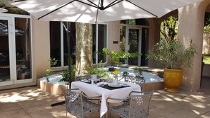 Eine Terrassensitzgruppe im Freien mit Esstisch, umgeben von Korbstühlen, unter einem großen Sonnenschirm.