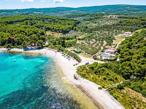 Vista aérea de una zona costera con playa, aguas turquesas cristalinas y vegetación circundante.