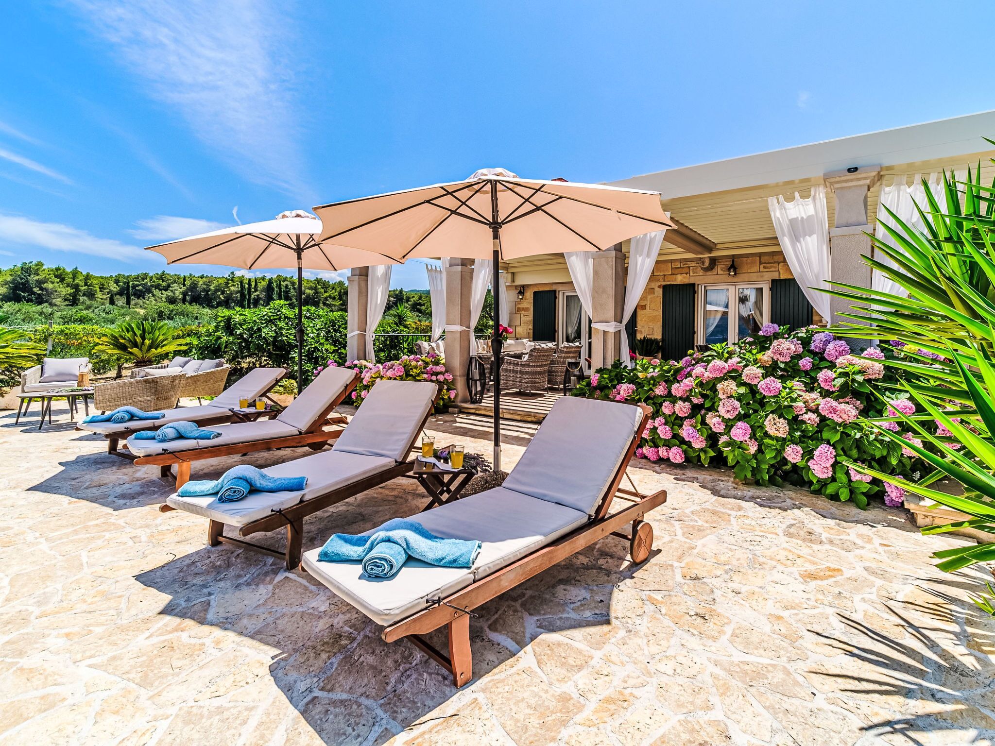Un espace aménagé au bord de la piscine, avec des chaises longues, des parasols et un sol recouvert de dalles de pierre.