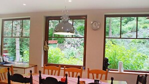 A dining area with a table and chairs, large windows with a view of greenery, a wall clock, and a hanging light fixture. - Karpacz Kowary by Interhome (Karpacz)