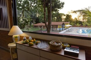 A kitchen counter with a window view of a swimming pool, a lamp, and various kitchen items. - Pousada Villa das Flores (Olímpia)