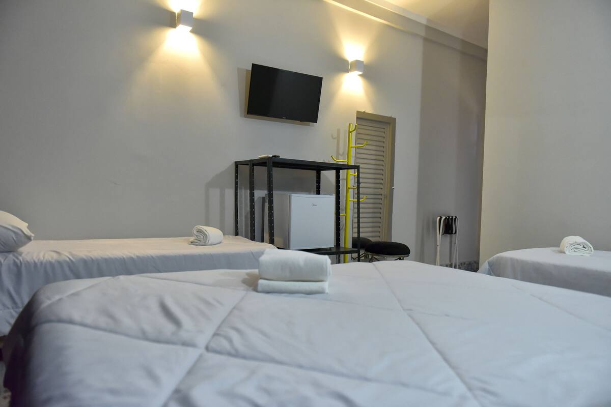 Habitación de hotel con dos camas, un televisor montado en la pared y una pequeña mesa con una silla.