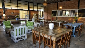 Un comedor amplio con mesas y sillas de madera, una pared de ladrillo y ventanas grandes.