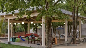 Zona de juegos al aire libre techada con tobogán, bancos y una hamaca.