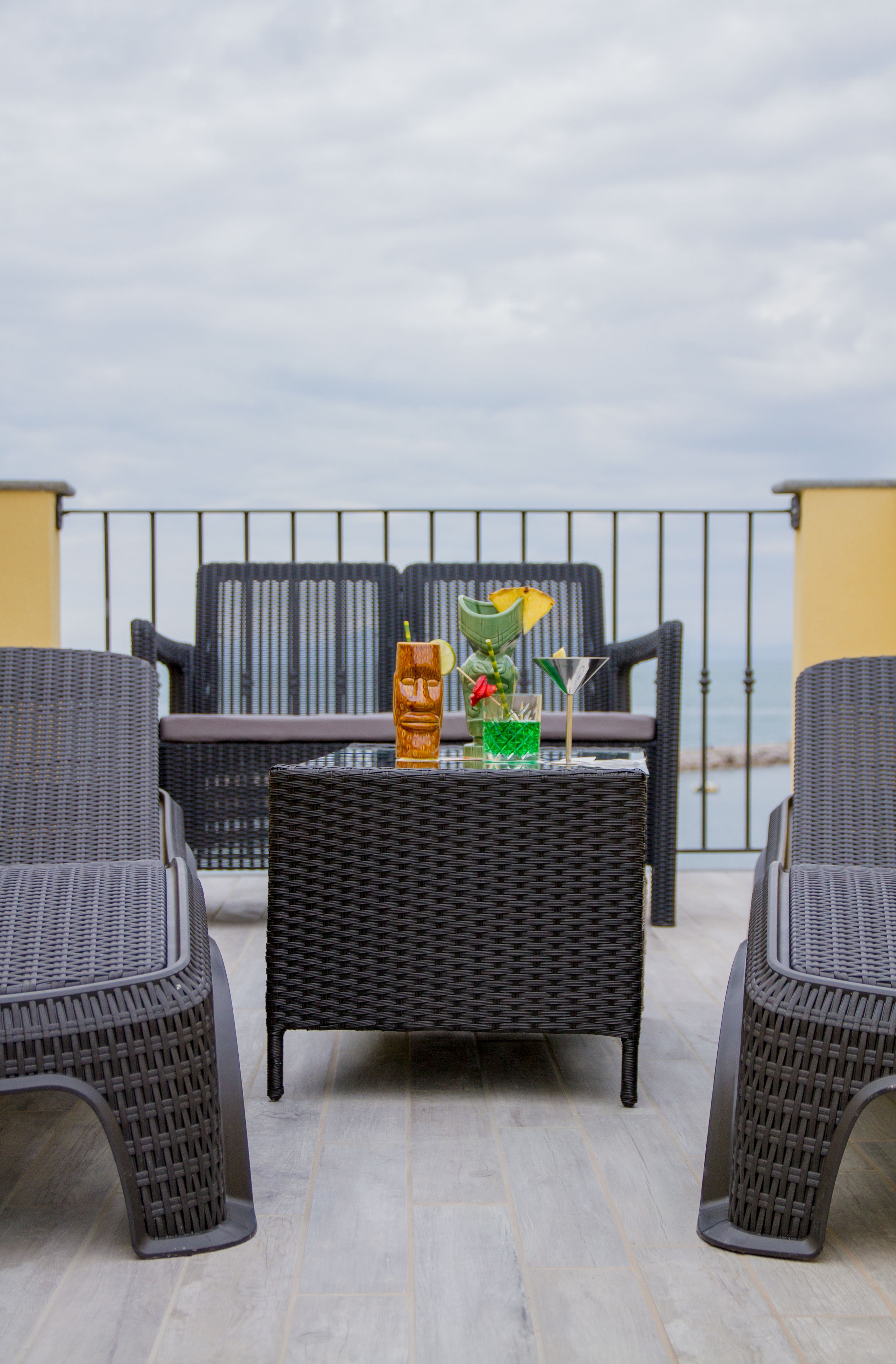 A balcony with wicker furniture and a table set with a drink, a flower, and a glass.