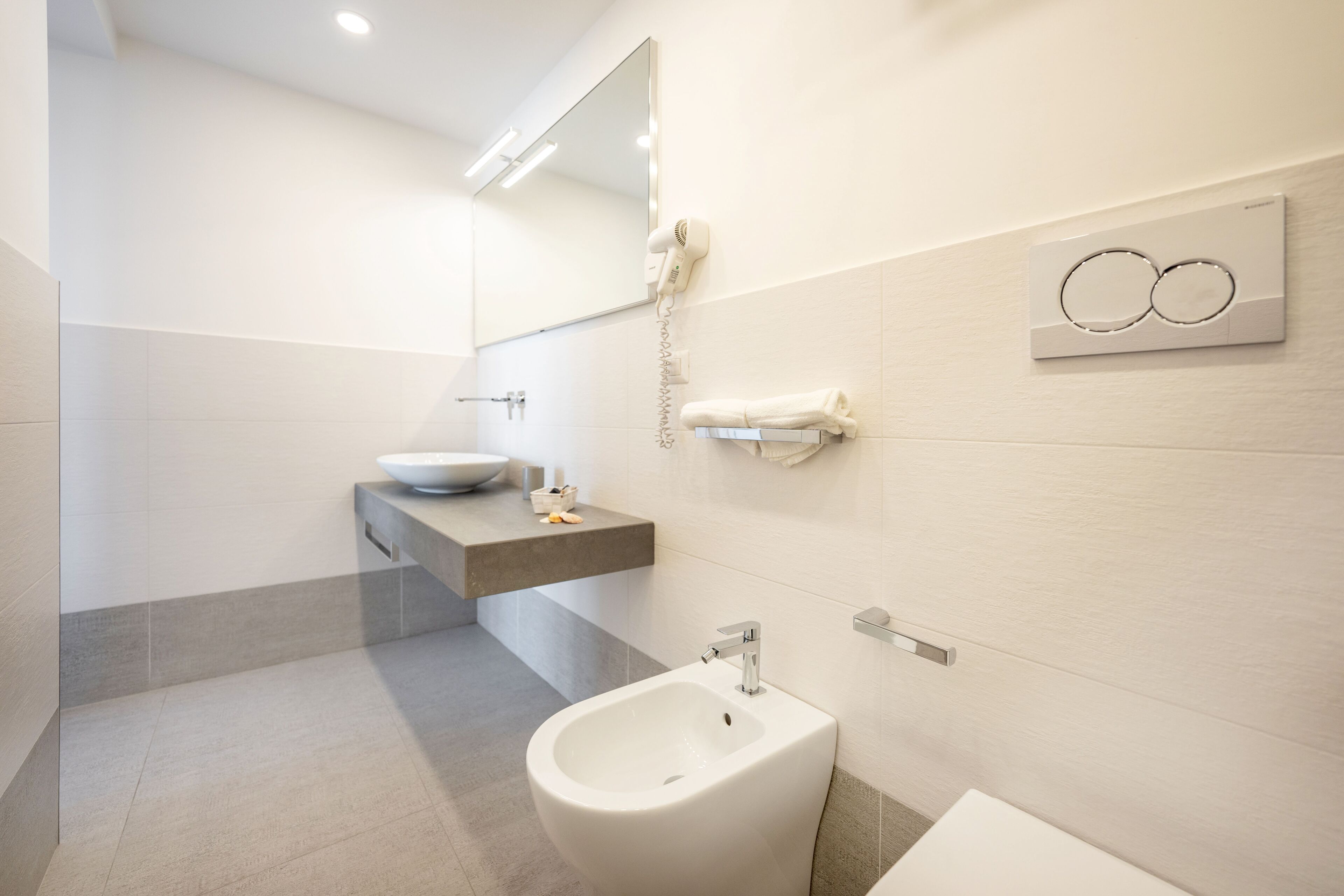 A modern bathroom with a bidet, a sink, a towel rack, and a hairdryer on the wall.