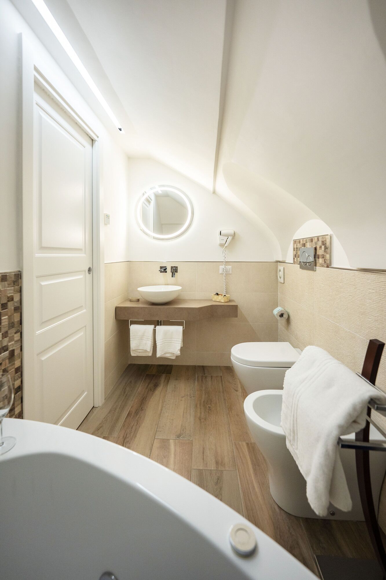 A modern bathroom with a freestanding bathtub, a round mirror, a toilet, and a vanity with a sink.