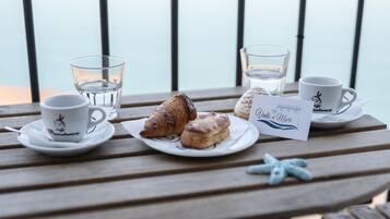 Una mesa de madera con un plato de pasteles, dos tazas, un vaso de agua, una decoración de estrella de mar y un letrero que dice "Vento di Mare".