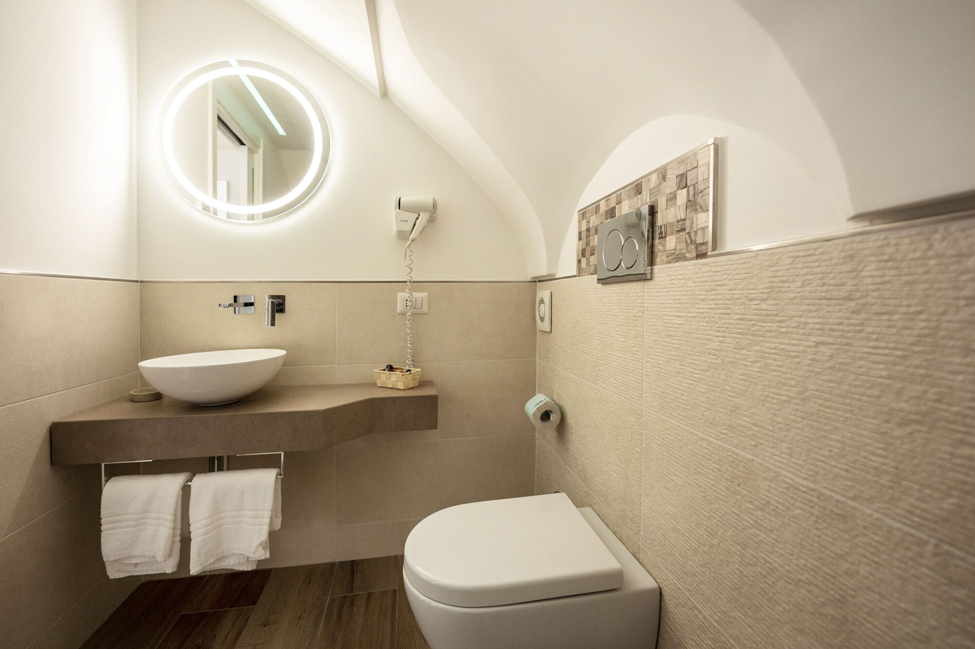 A modern bathroom with a round mirror, a white sink, a toilet, and a towel rack.