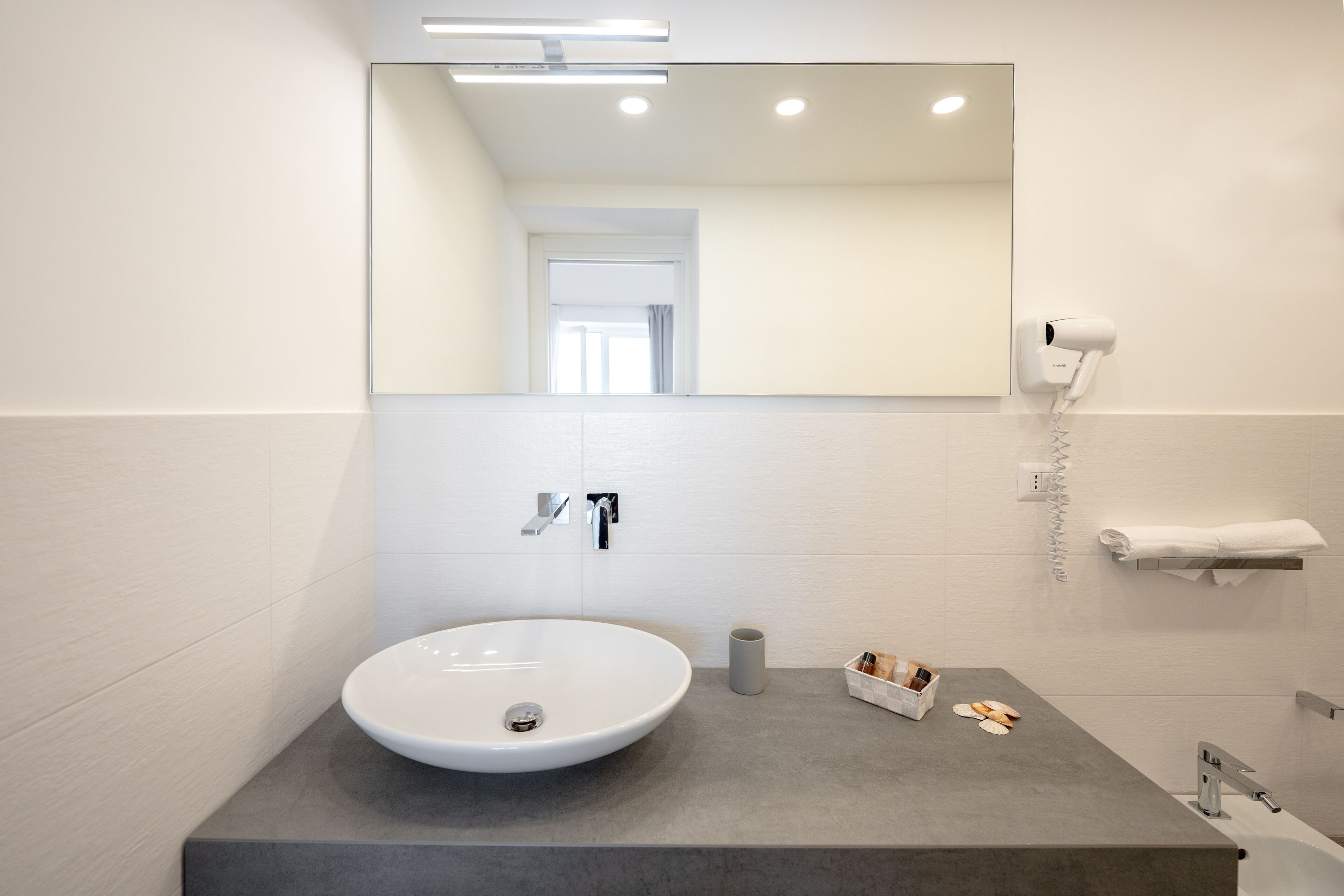 A modern bathroom with a large white sink, a mirror, a hairdryer, and a towel rack.