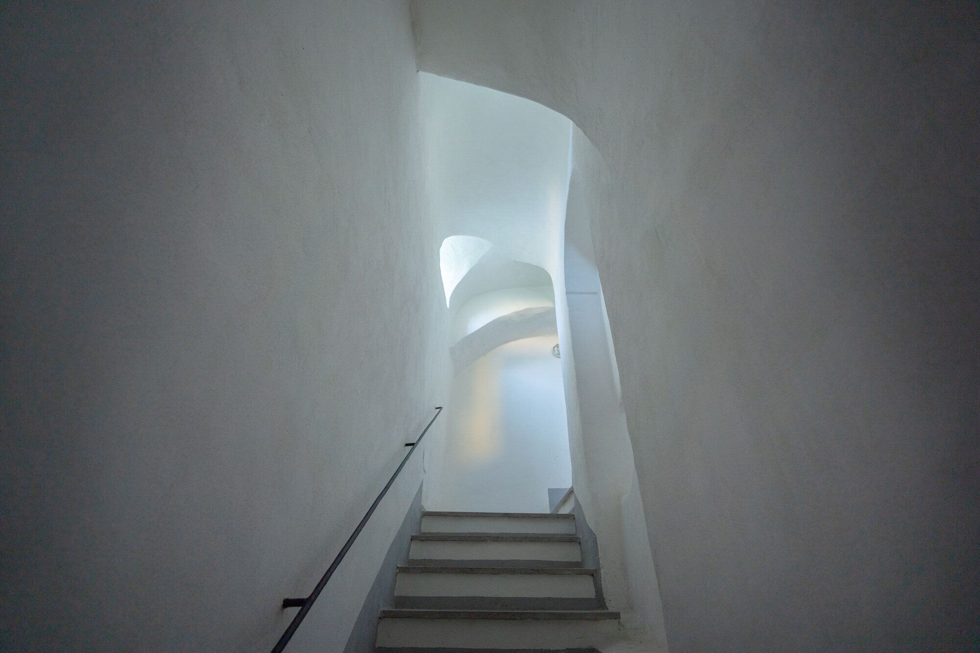 Una escalera de diseño moderno que asciende por un estrecho pasillo de paredes blancas.