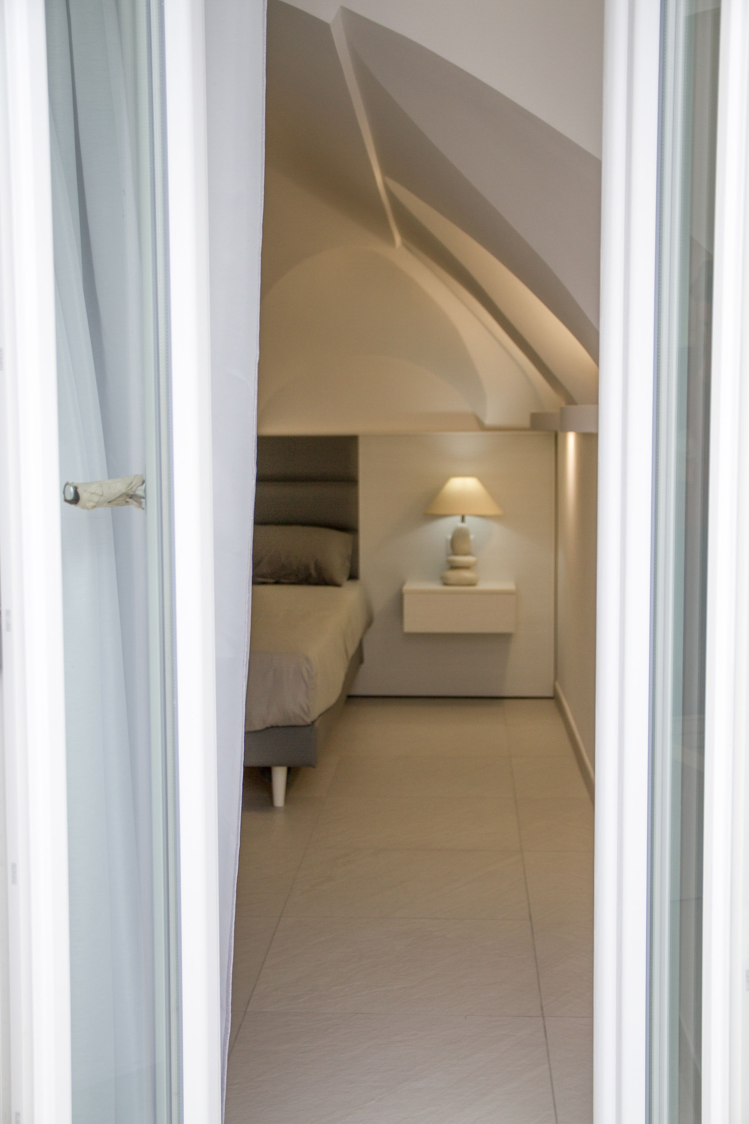 Un estrecho pasillo que conduce a un dormitorio con una cama, una mesita de noche y una lámpara.