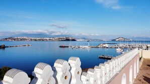 Un puerto costero con barcos amarrados, una cerca blanca con arcos y un pueblo al fondo.