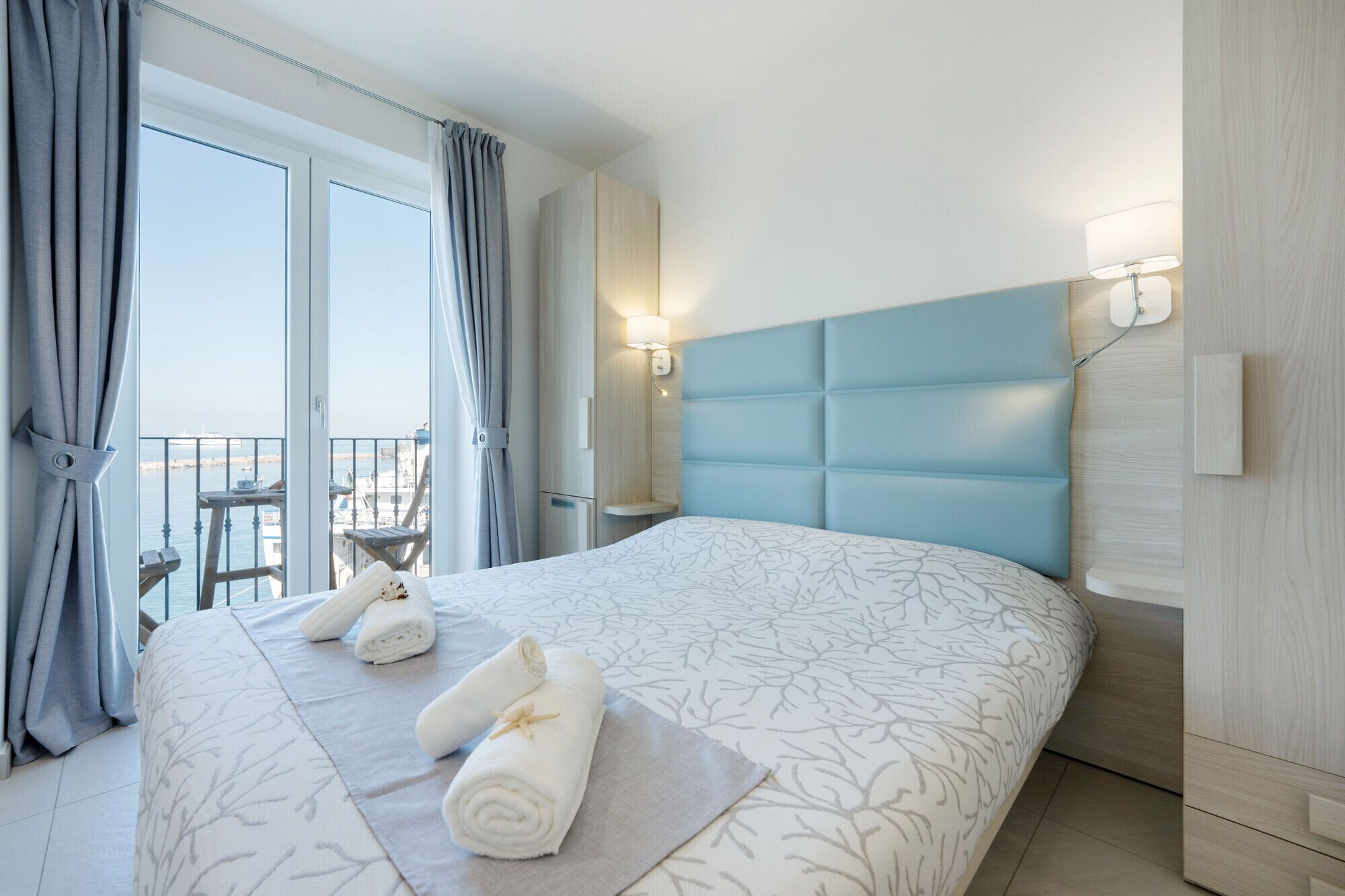 A hotel room with a large bed, a balcony with a view, and a wall-mounted light fixture.