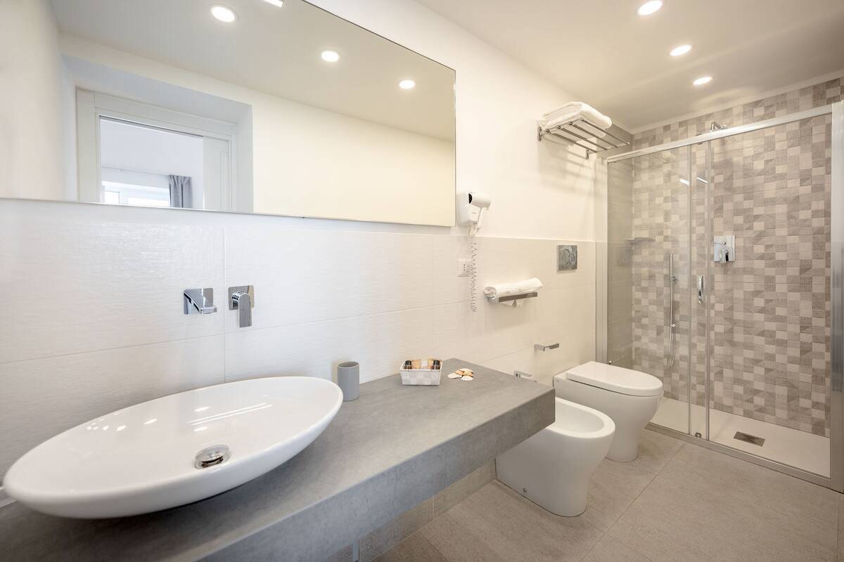 Un baño moderno con un lavamanos ovalado grande, un inodoro y una ducha con mampara de vidrio.