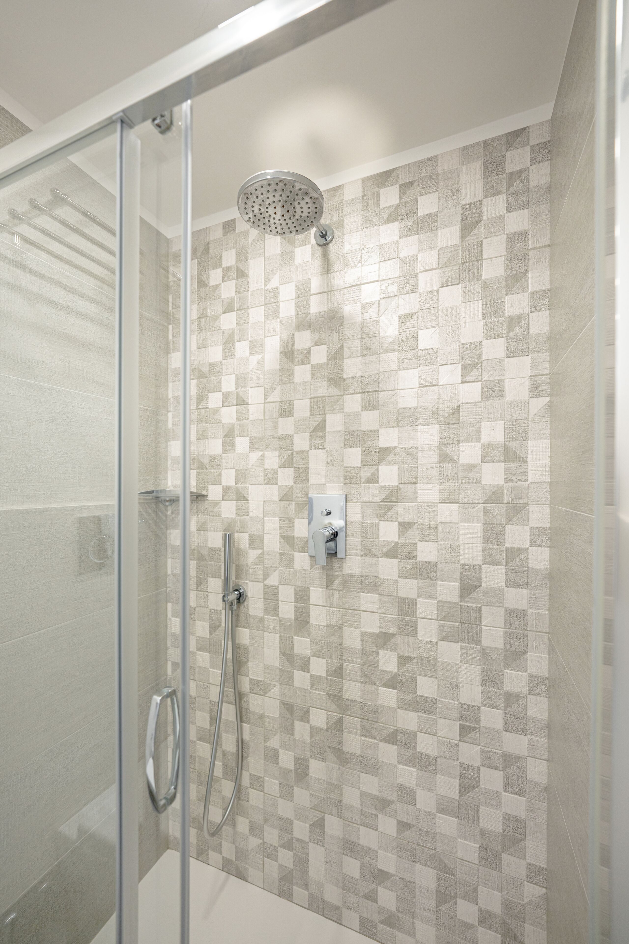 Dusche mit Glastür, Regendusche und einer gefliesten Wand mit geometrischem Muster.