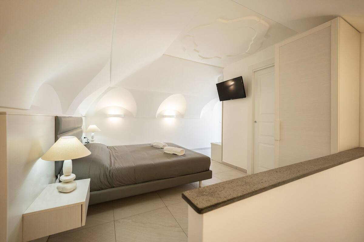 Un dormitorio moderno con cama, lámpara de noche y televisor de pantalla plana montado en la pared.