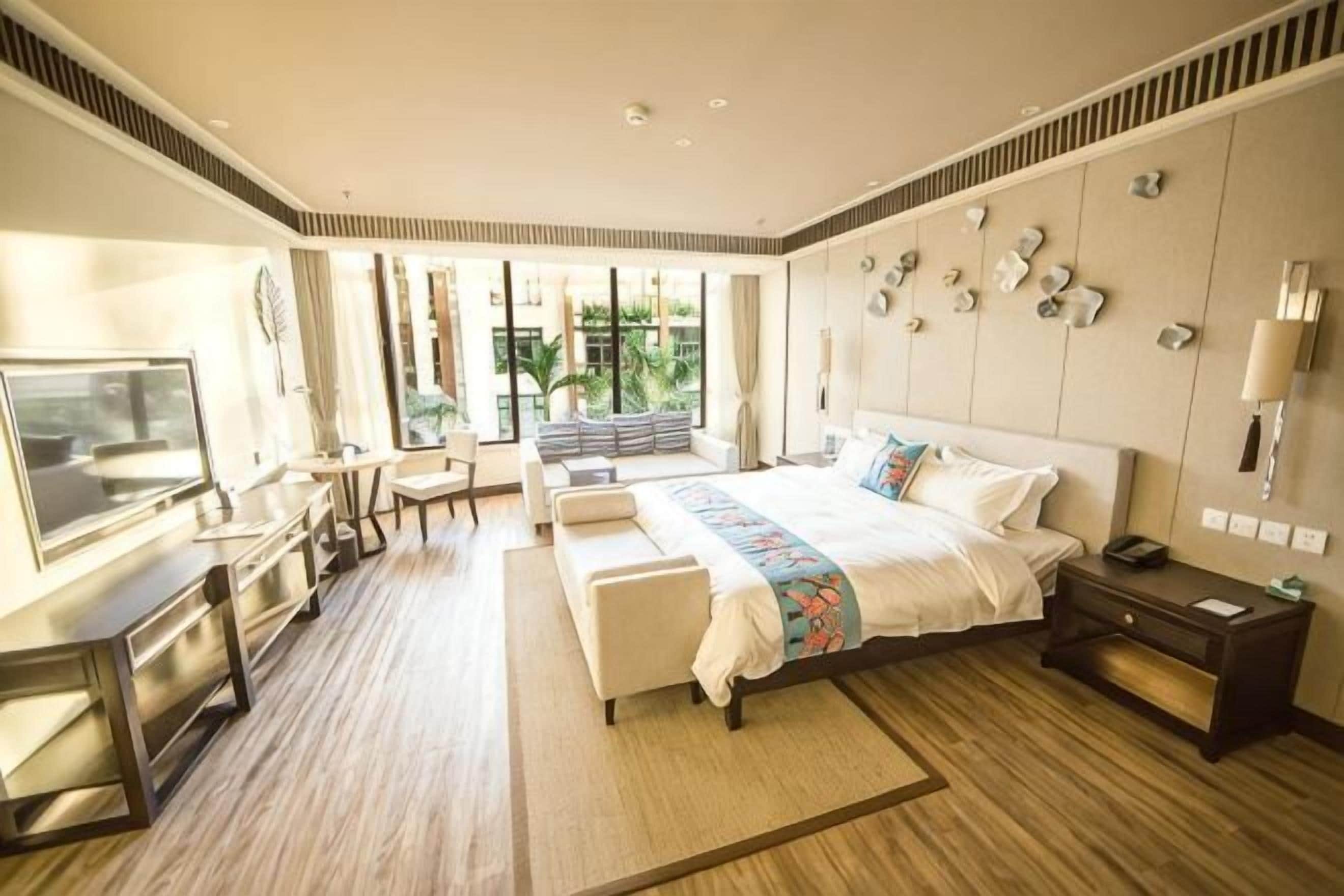 Una habitación de hotel moderna con una cama grande, un escritorio, un televisor y vistas a zonas verdes.