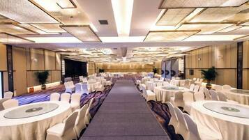 A banquet hall with rows of round tables, chairs, and a carpeted floor.