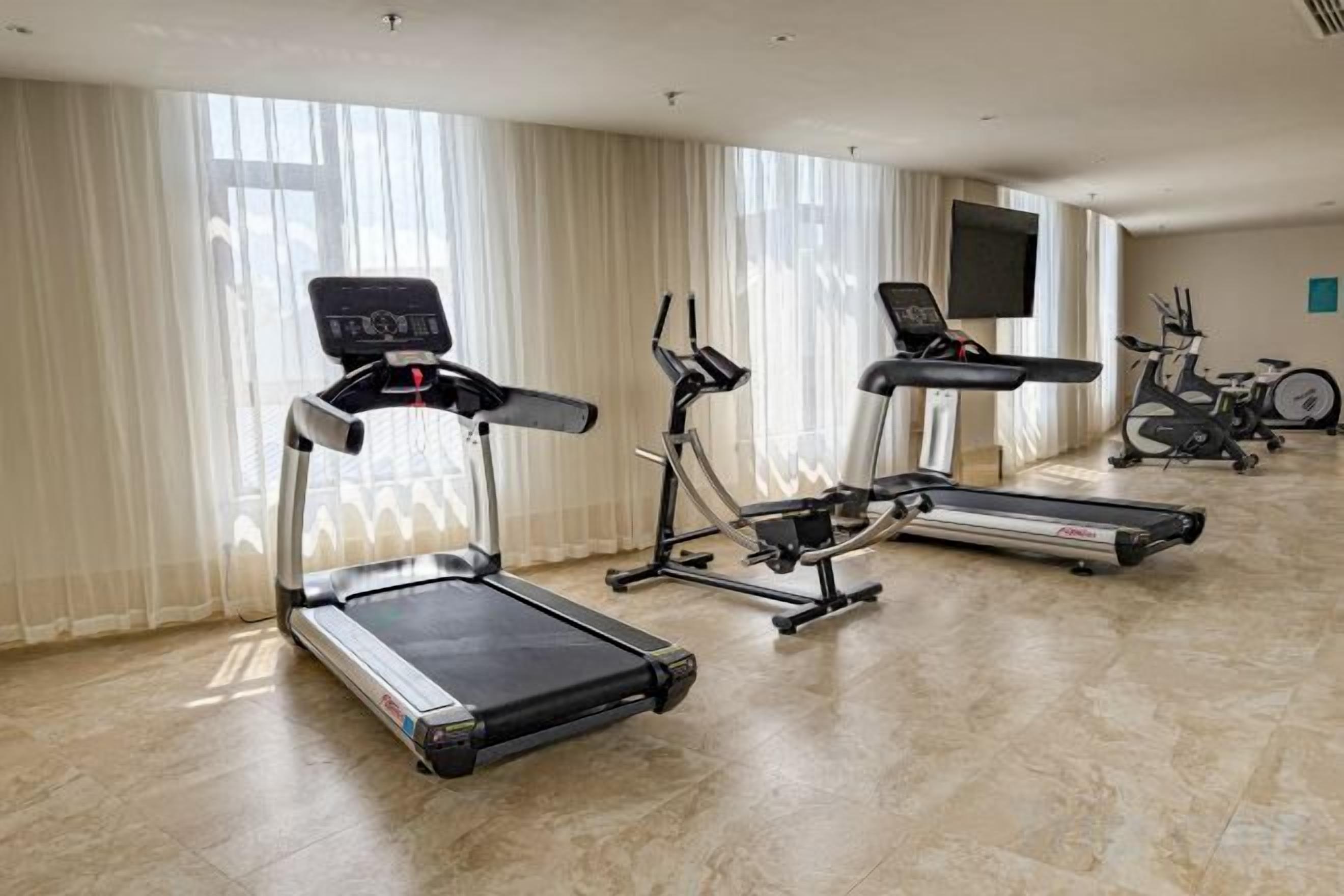 Una palestra attrezzata con tapis roulant, biciclette fisse e uno schermo televisivo.