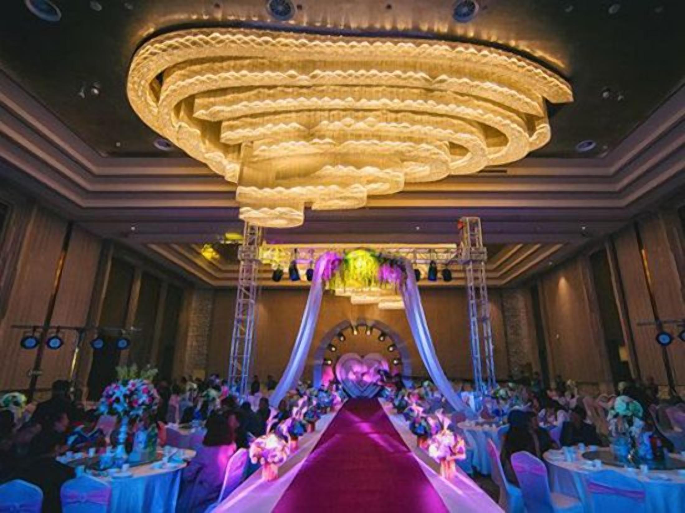 A grand hall with a central aisle, ornate chandeliers, and tables set for an event.