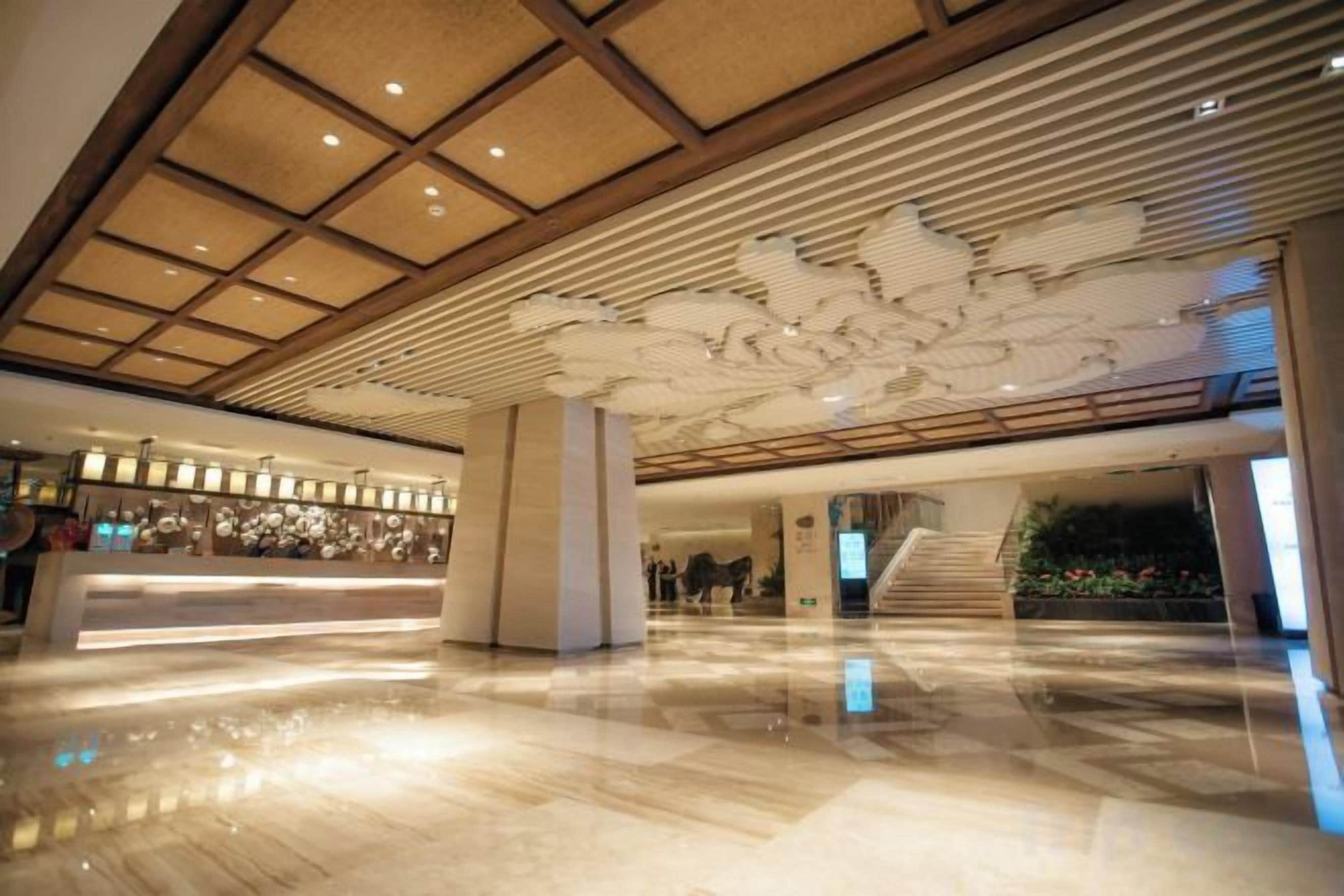 A spacious lobby with a reception desk, a staircase, and a large decorative ceiling.