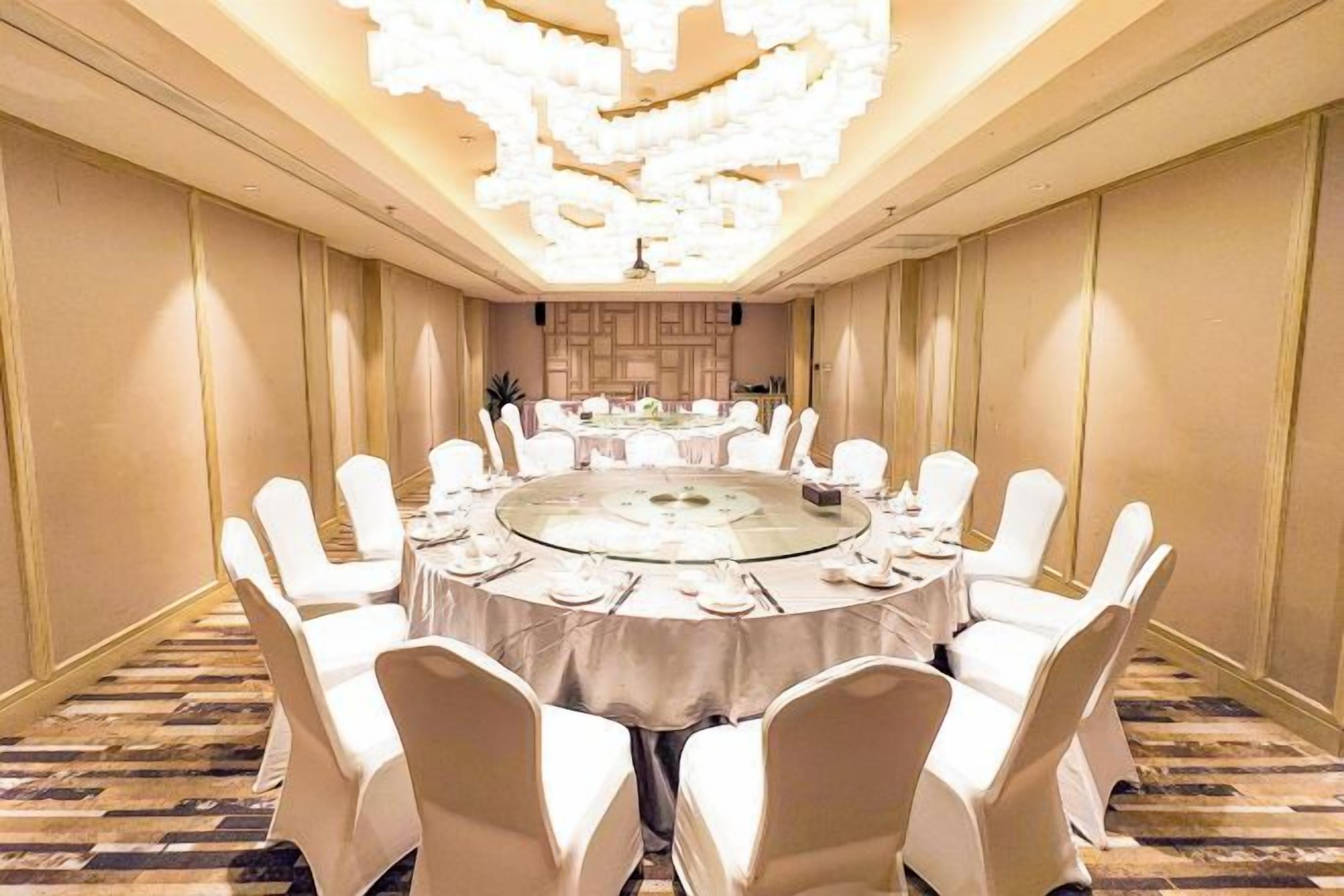 A conference room with a round table, white chairs, and a chandelier.