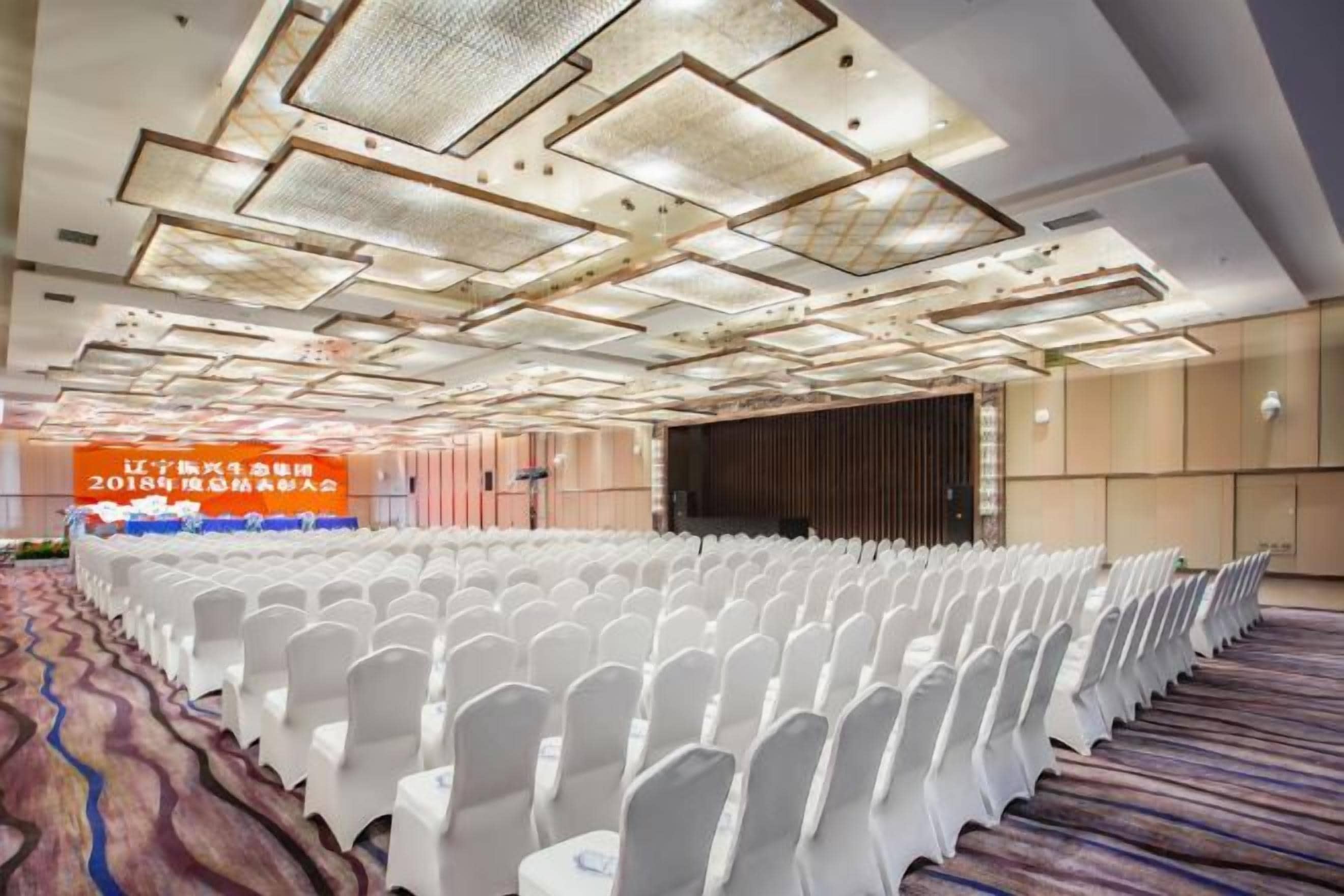 A conference room with rows of white chairs, a stage, and a large banner.