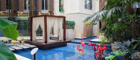 A pool area with a glass-enclosed seating area, surrounded by tropical plants and a decorative flamingo statue.