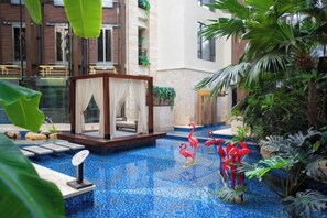 Un área de piscina con un espacio de estar de vidrio, rodeado de plantas tropicales y una estatua decorativa de flamenco.