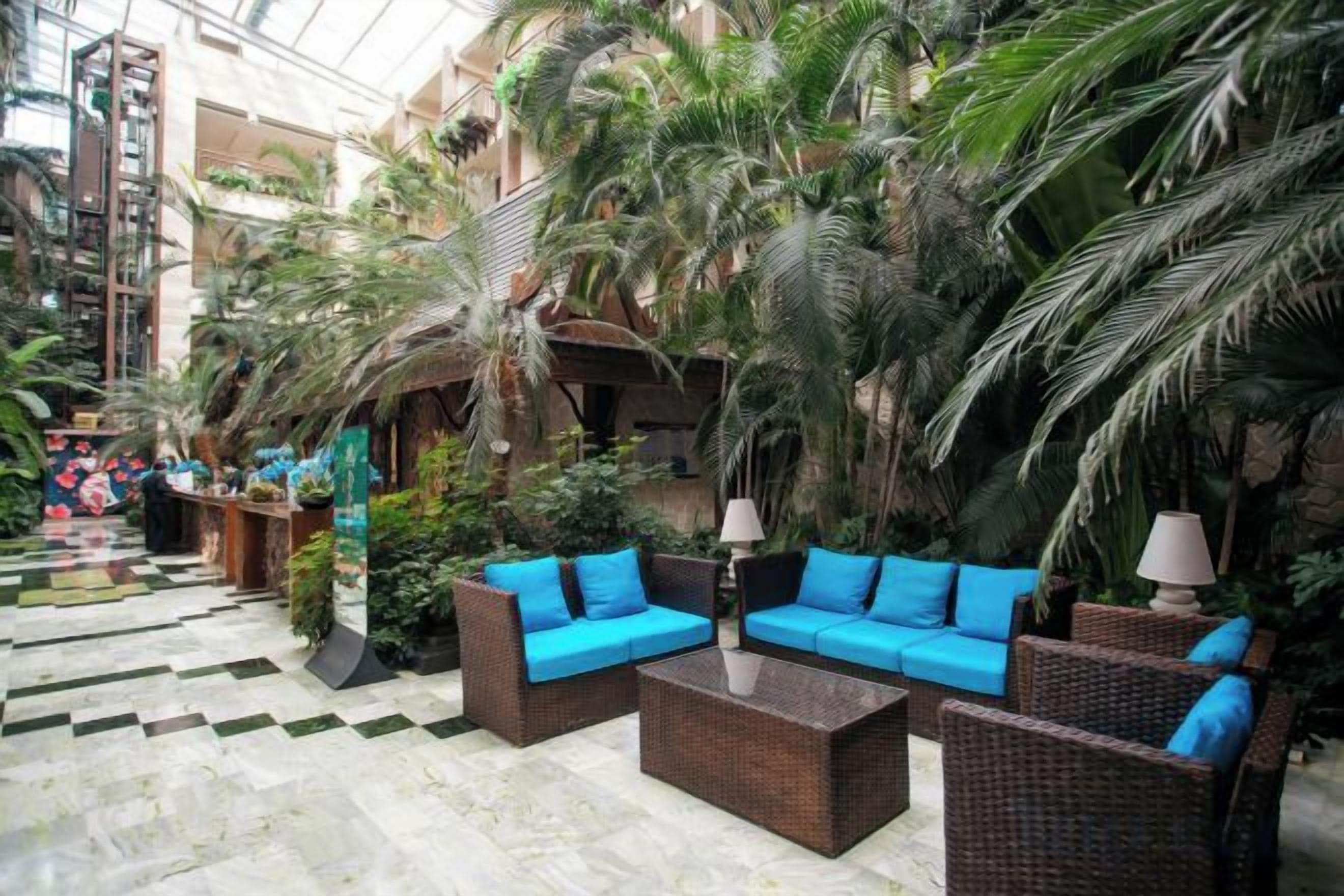Un atrium intérieur aménagé avec des meubles en osier, des palmiers et un sol à carreaux.