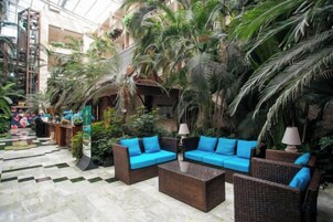 An indoor atrium with wicker furniture, palm trees, and a checkered floor.