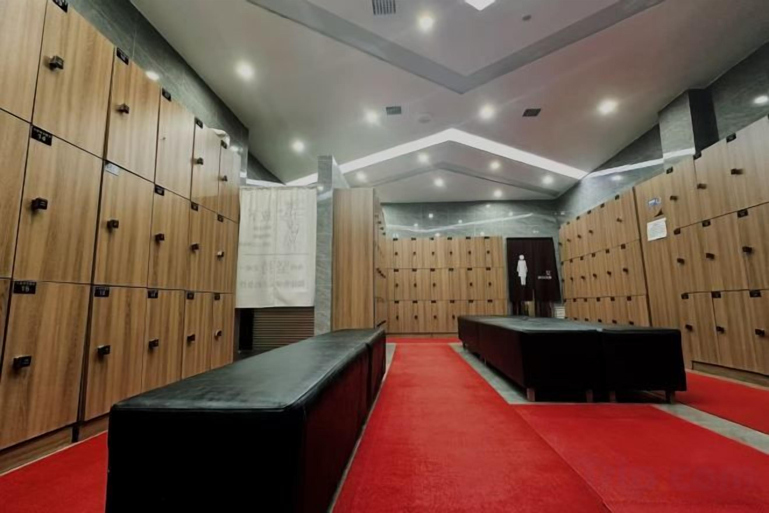Un vestuario con varios taquillones de madera, un banco negro y una alfombra roja.