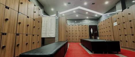 Un vestuario con varios taquillones de madera, un banco negro y una alfombra roja.