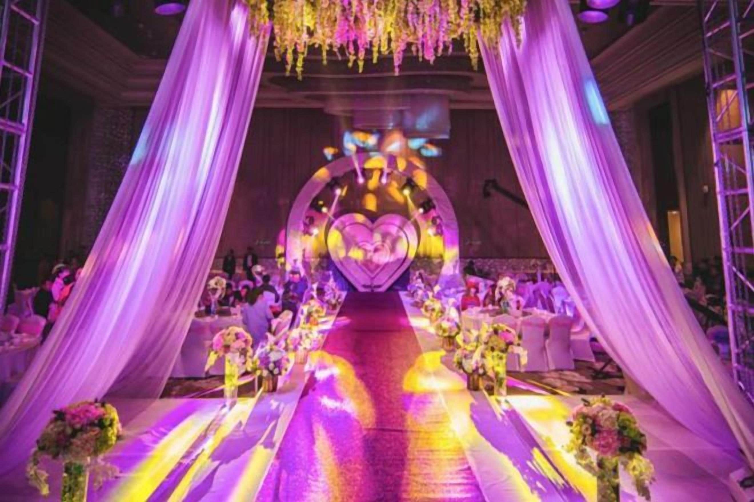 Un espacio para eventos en interiores con un pasillo central, cortinas decorativas y arreglos florales.