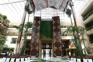 A spacious atrium with a high ceiling, large wooden doors, and a central water feature.
