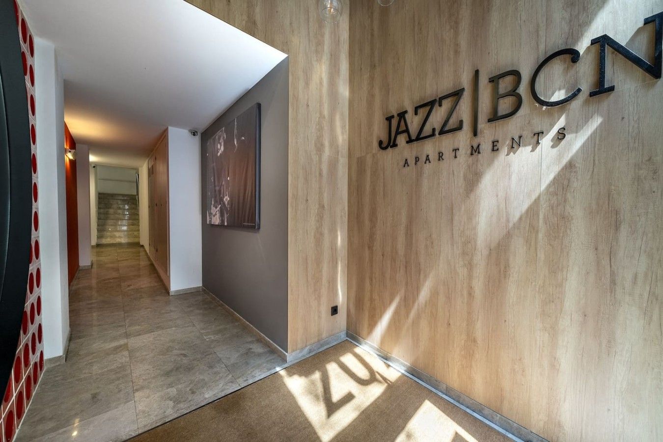 Un couloir avec un mur en bois sur lequel est affiché l’enseigne « JAZZ BCN APARTMENTS », qui mène à un escalier.