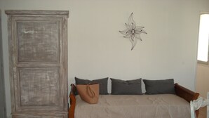 A room with a wooden wardrobe, a beige sofa with pillows, and a wall-mounted decorative piece. - LA GARIGUETTE APARTMENT NEAR NIMES (Uchaud)