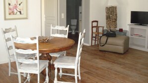 A dining area with a wooden table and white chairs, a television on a stand, and a sofa in a living room. - LA GARIGUETTE APARTMENT NEAR NIMES (Uchaud)
