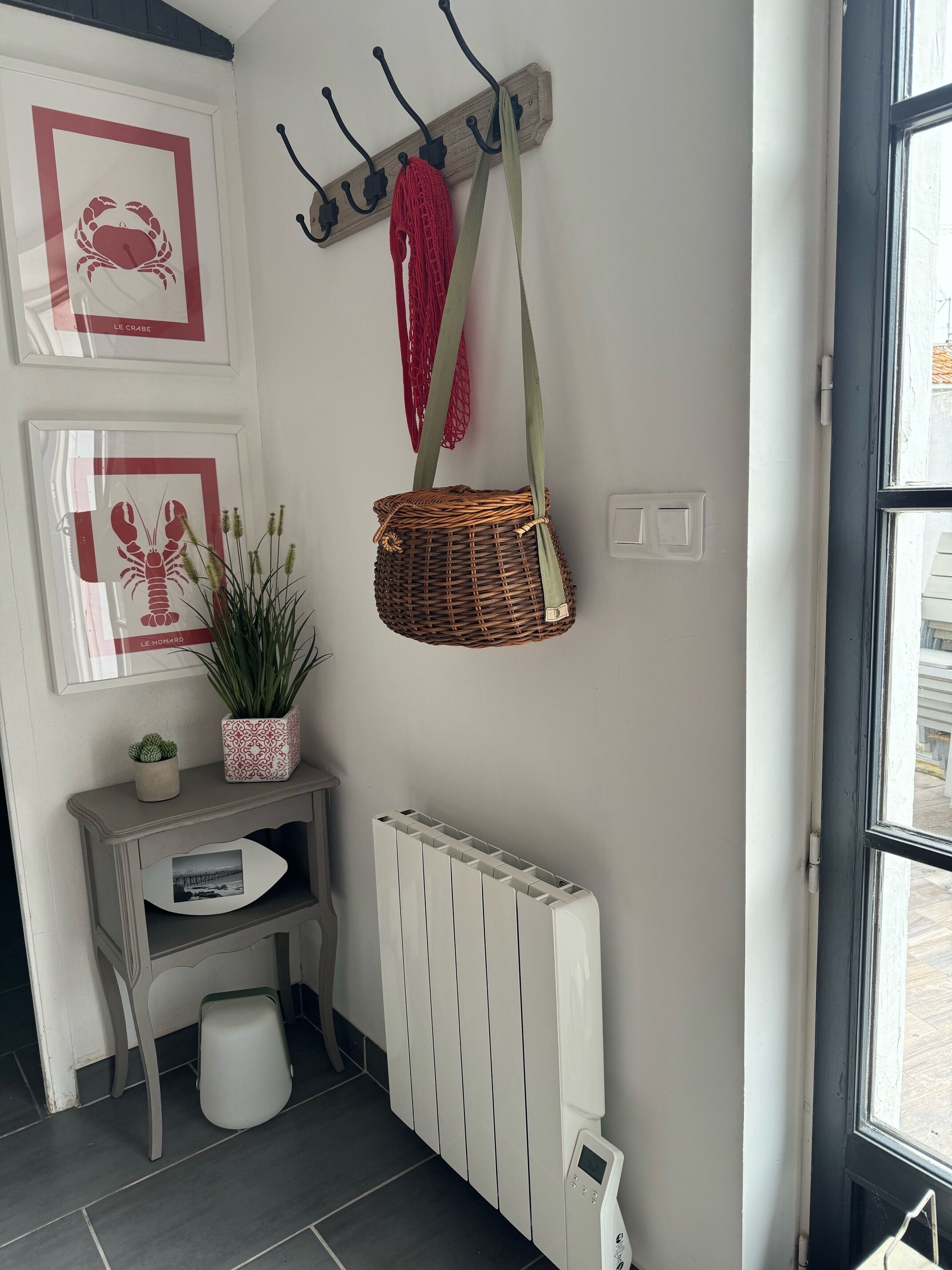 Un racó d'una habitació amb un radiador, una taula petita amb una planta i un penjador fixat a la paret amb un borsa vermella.