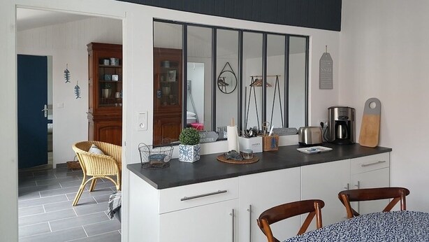 Cocina moderna con encimera negra, armarios blancos y un espejo grande. Hay una zona de comedor con dos sillas y una mesa.