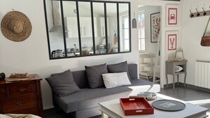 Una sala de estar moderna con un sofá gris, un sillón blanco, un aparador de madera y una mesa de comedor con una bandeja roja.