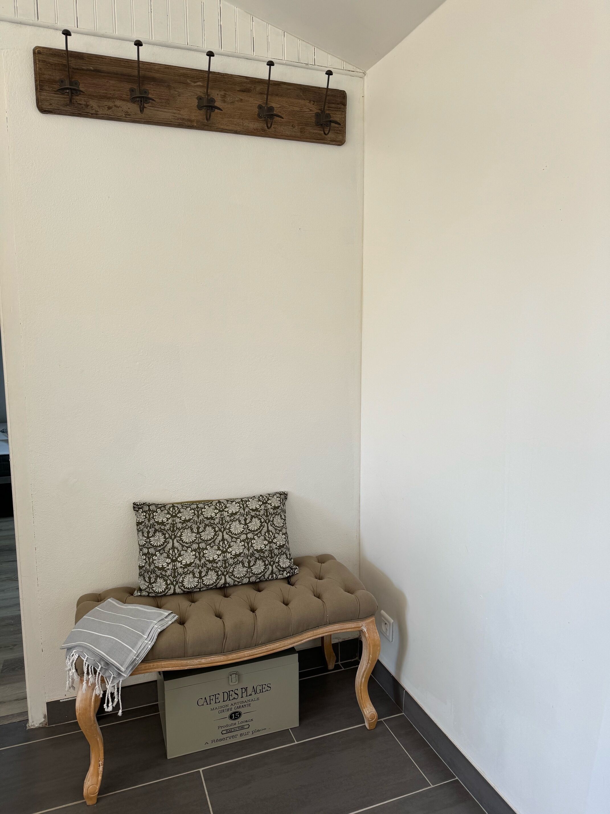Un rincón amoblado con un banco acolchado, un cojín estampado y un estante de madera fijado a la pared.