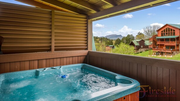 Un jacuzzi en una cabaña de madera con vistas a una montaña y un edificio rojo al fondo.