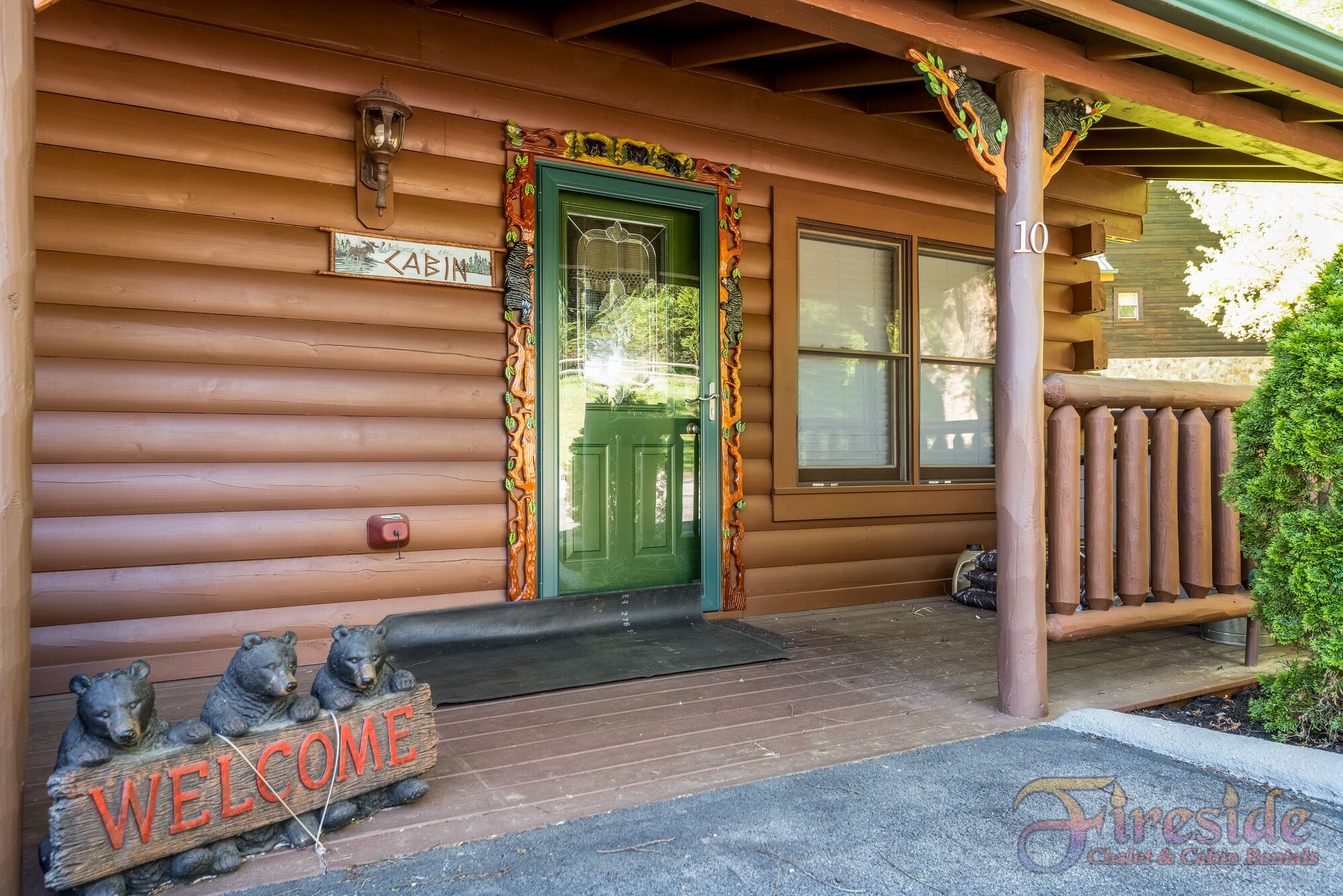 A cabin with a green door, a 'Welcome' sign, and a 'Cabin' sign above the door.