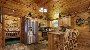 Cocina de cabaña de madera con refrigerador, microondas, horno y taburetes de bar de madera.